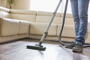 Sección baja del hombre limpiando piso de madera dura con aspirador