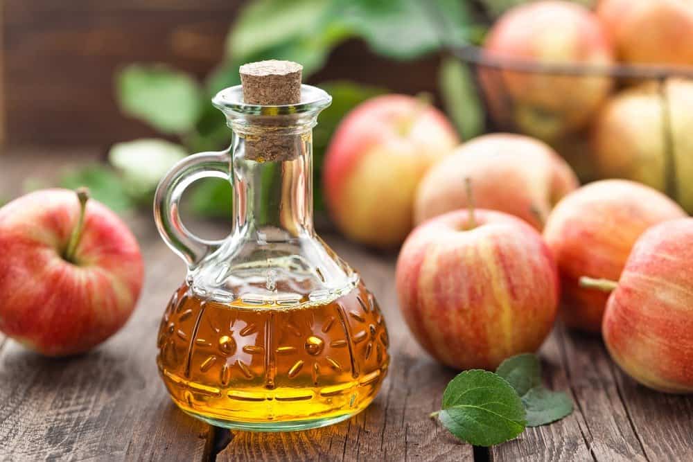 Manzanas y un tazón de manzana Vinagre sobre mesa de madera